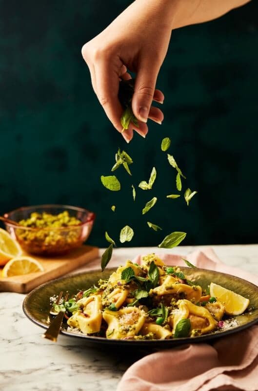 Fresh herbs being sprinkled over a plate of pasta with peas and lemon