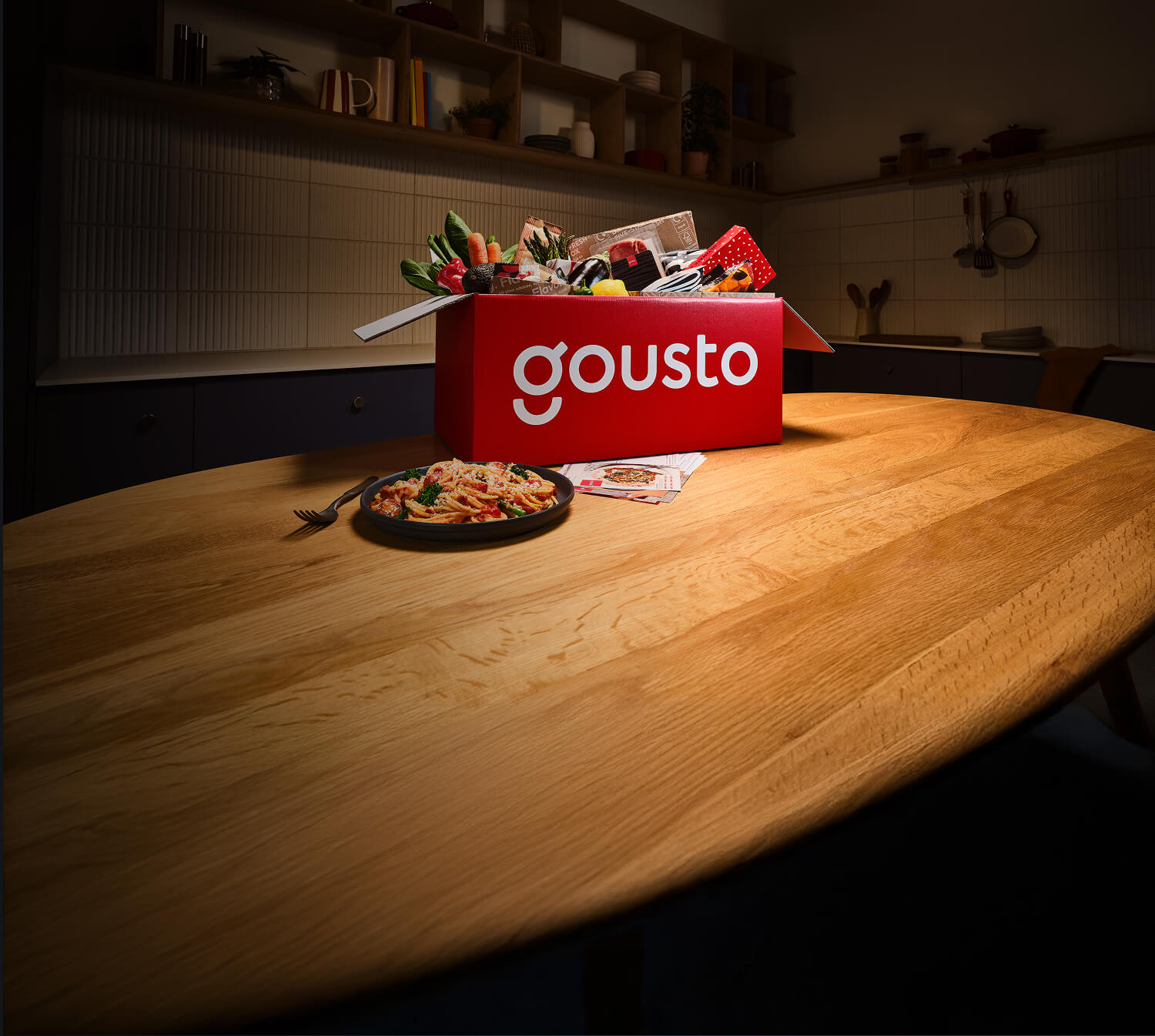 A kitchen counter with a Gousto box overflowing with fresh ingredients and a plated meal